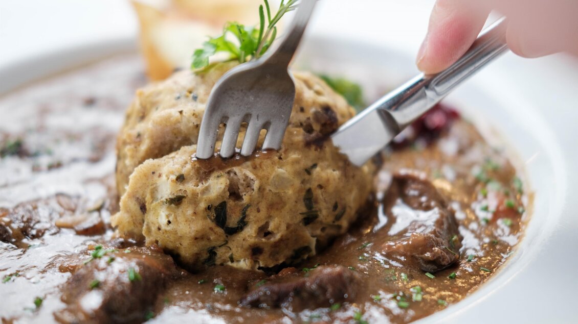 Ein Teller mit Fleisch und einer großen Knödel. Die Speise ist in einer dunklen Sauce angerichtet und sieht appetitlich aus. | © Bergstadl