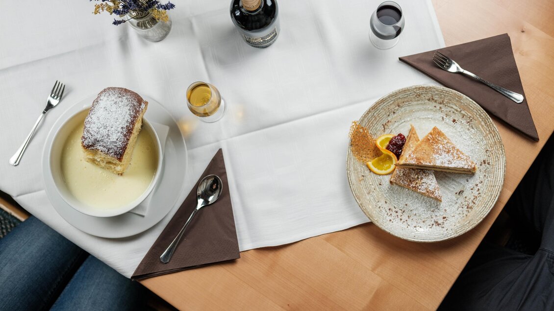Ein Tisch gedeckt mit köstlichem Essen, darunter ein Stück Kuchen und eine Dessertschale. Dazu sind Getränke und dekorative Details wie eine kleine Blumenvase zu sehen. | © Bergstadl