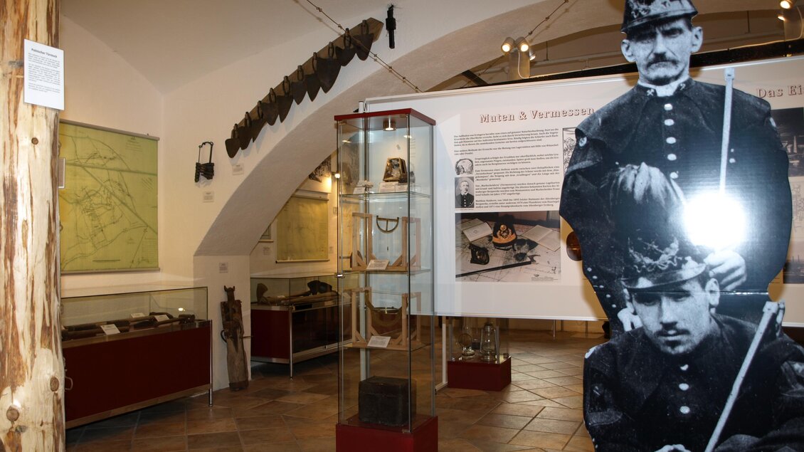 Ein Museum mit historischen Exponaten und einer Wandgrafik von Soldaten. Im Hintergrund sind Ausstellungsstücke in Vitrinen zu sehen.