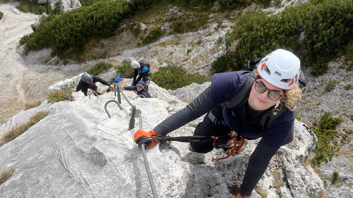 Eine Gruppe von Kletterern erklimmt eine Felswand in einer malerischen Berglandschaft. Die Kletterer sind gut gesichert und die Umgebung ist von Bäumen und Bergen geprägt. | © Best Adventure Company