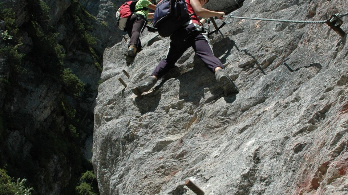 Zwei Kletterer, die einen steilen Felsen erklimmen. Die Umgebung ist von grünen Bäumen und blauen Himmel umgeben. | © Best Adventure Company