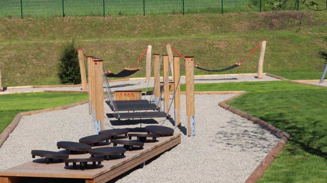 Ein moderner Spielplatz mit Holzstrukturen und Schaukeln. Der Platz ist von Rasen und Kies umgeben und bietet Spielmöglichkeiten für Kinder. | © Robert Cescutti