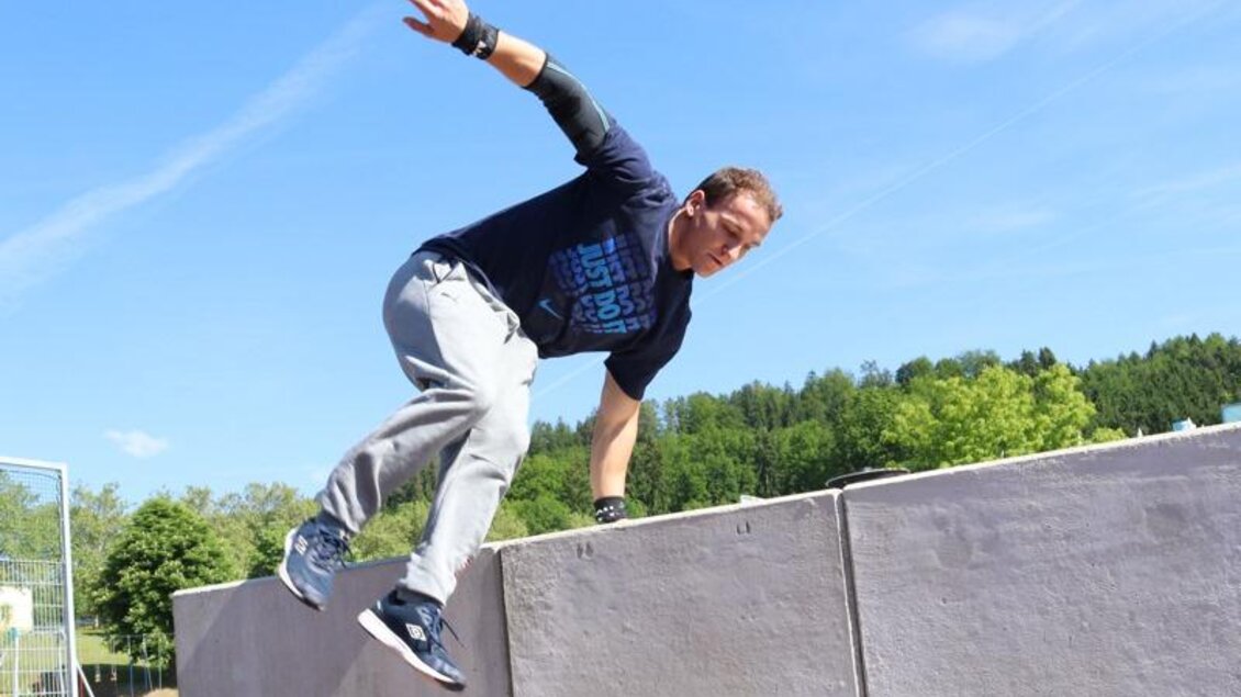 Ein Mann springt über eine Mauer in einem Park. Der Himmel ist blau und es ist sonnig. | © Robert Cescutti