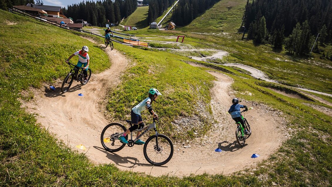Eine Gruppe von Radfahrern fährt auf einem kurvenreichen Trail in einer schönen, grünen Landschaft. Im Hintergrund sind Wälder und Hügel zu sehen. | © Roland Haschka
