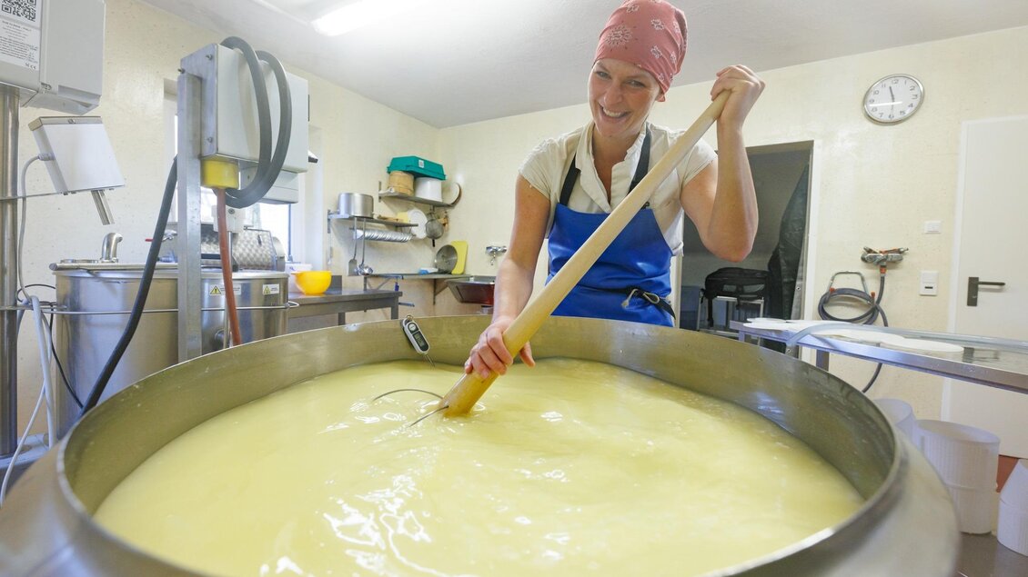 Eine lächelnde Frau rührt in einem großen Topf mit frischer Käsemischung. Der Raum ist hell und gut ausgestattet für die Käseherstellung. | © Engelhardthof