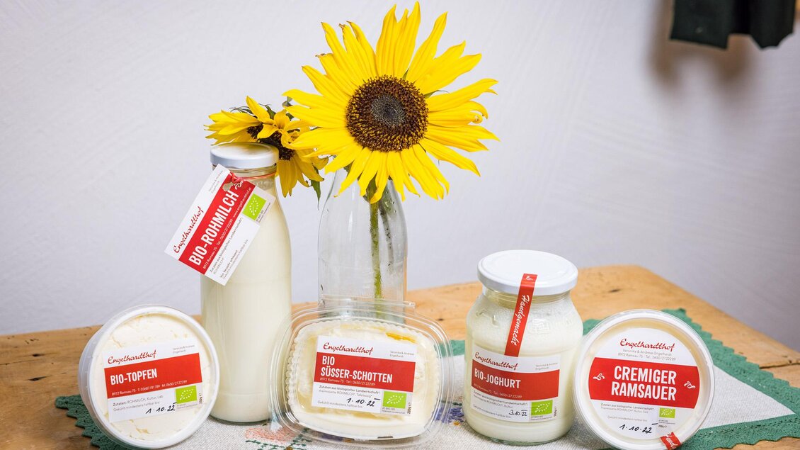 Eine Auswahl an Milchprodukten in verschiedenen Behältern, platziert auf einem Tisch. Neben den Produkten steht eine fröhliche Sonnenblume. | © Netzwerk Kulinarik wildbild