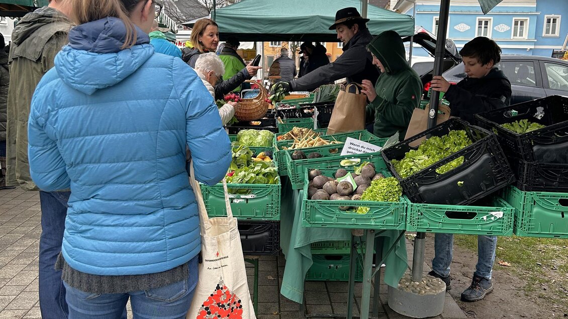 Ein Marktplatz mit mehreren Ständen, die frisches Obst und Gemüse anbieten. Menschen kaufen ein und genießen die lokale Atmosphäre. | © TVB Murau
