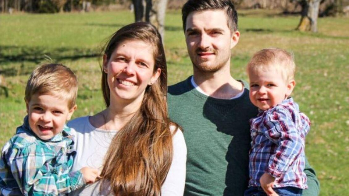 Eine glückliche Familie steht in einem grünen Feld. Die Eltern halten ihre zwei kleinen Kinder in den Armen und strahlen Freude aus. | © Lienlbauer