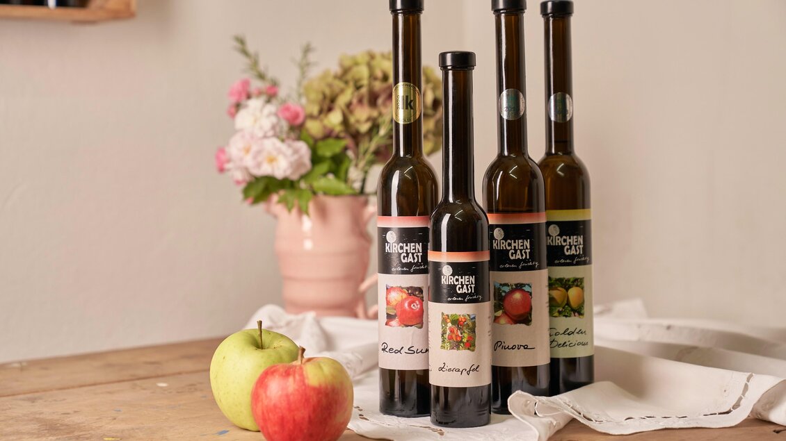 Vier Flaschen mit Fruchtsäften stehen auf einem Holztisch. Neben den Flaschen liegen ein grüner und ein roter Apfel sowie eine Vase mit Blumen. | © Philipp Monihart