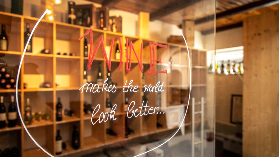 Ein Innenraum mit einer Holzregalwand, auf der Weinflaschen stehen. Ein Schriftzug sagt: „Wine makes the world look better...“. | © TV Region Graz - Lunghammer