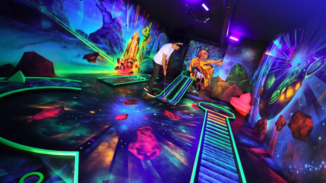 Ein aufregendes Minigolf-Erlebnis in einem leuchtend bunten, futuristischen Raum. Die Wände sind mit sci-fi Motiven dekoriert, die eine galaktische Atmosphäre schaffen. | © Black Light Minigolf