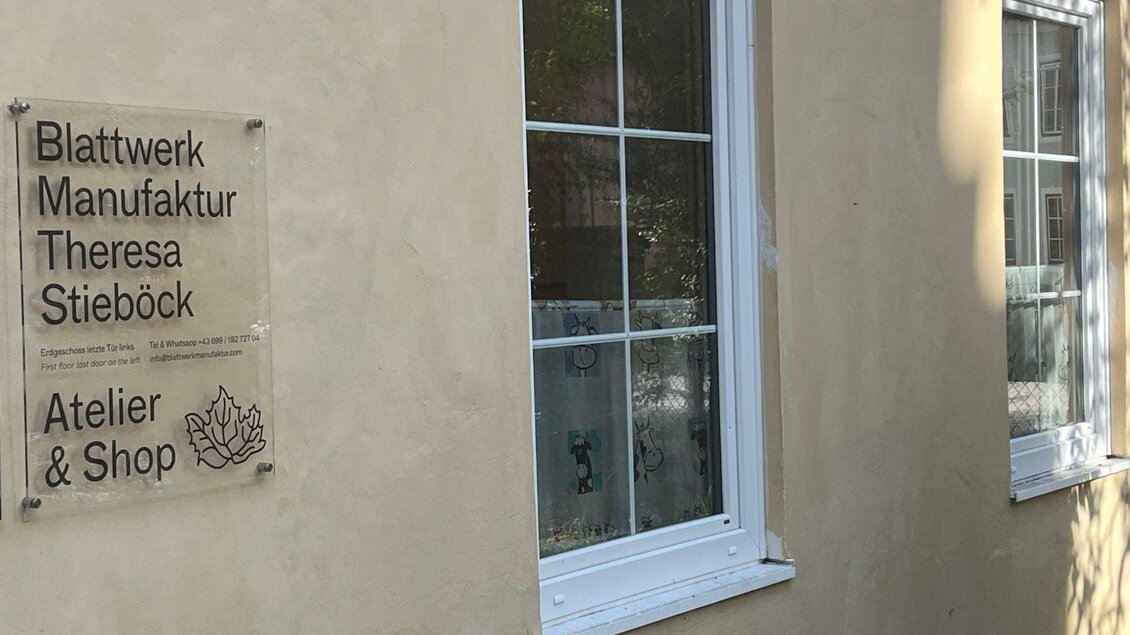 Ein Atelier und Shop mit der Aufschrift „Blattwerk Manufaktur Theresa Stieböck“ ist an einer hellen Wand zu sehen. Neben der Tür gibt es ein Fenster mit einem schlichten Design. | © TVB Ausseerland Salzkammergut_Nathalie Schröttenhamer