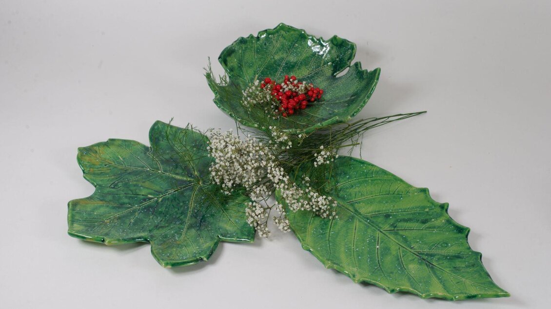 Eine dekorative Schale in Form von Blättern in verschiedenen Grüntönen. Darin befinden sich rote Beeren und kleine weiße Blumen. | © Blattwerk Manufaktur, Theresa Stieböck