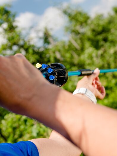 A person aims with a bow and arrow in a green environment. In the background, a target is visible. | © Mias Photoart