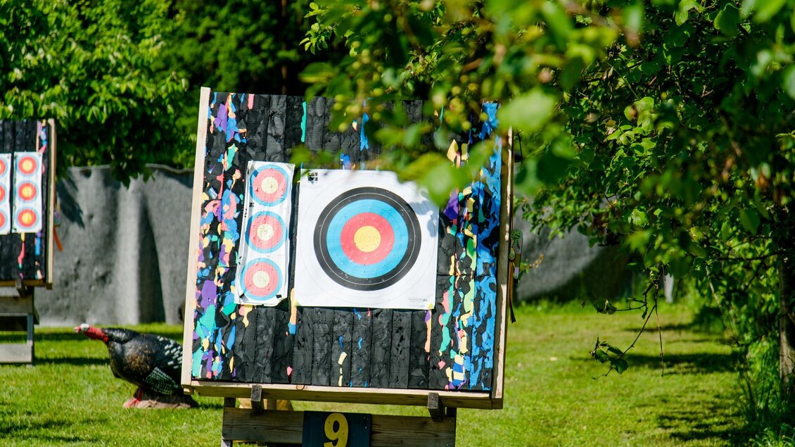 Eine Zielscheibe steht auf einem Gestell in einem grünen Garten. Im Hintergrund sind weitere Zielscheiben und eine natürliche Umgebung zu sehen. | © Mias Photoart