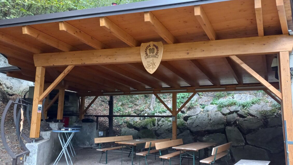Ein überdachter Holzpavillon mit Bänken und Tischen. Im Hintergrund sind Felsen und Bäume zu sehen. | © Bogenschützen Obervoitsberg-Artner