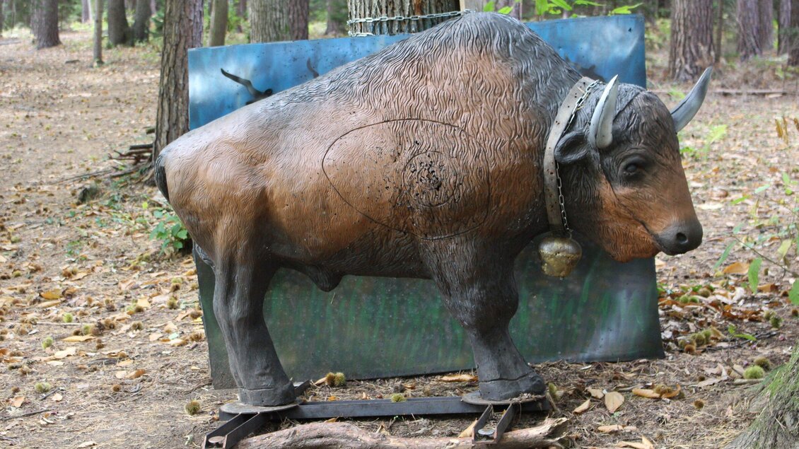Eine Holzskulptur eines Bisons steht in einem Wald. Der Hintergrund ist grün und zeigt Bäume. | © Archery Freaks - Frahs