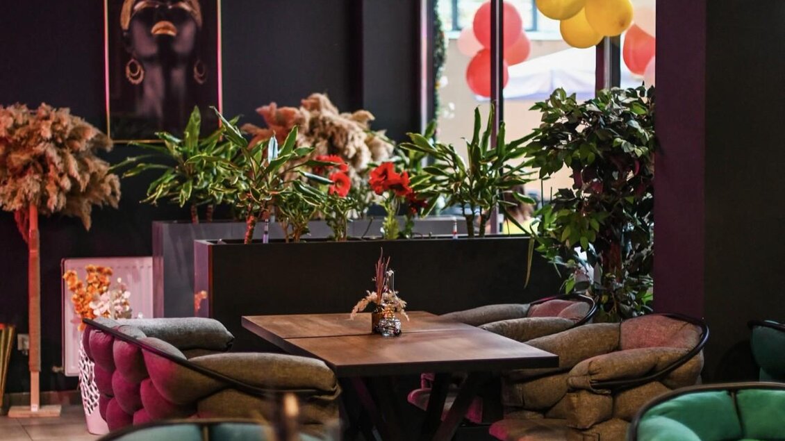 Ein stilvolles Café mit gemütlichen Sitzecken und vielen Pflanzen. An den Wänden hängen dekorative Kunstwerke und bunte Luftballons sorgen für eine freundliche Atmosphäre. | © Bonbon