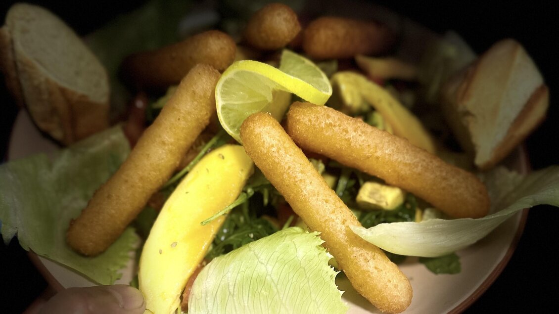 Ein bunter Salat mit knackigem Gemüse, frittierten Snacks und Zitronenscheiben. Das Gericht wird auf einem runden Teller serviert. | © Bonbon