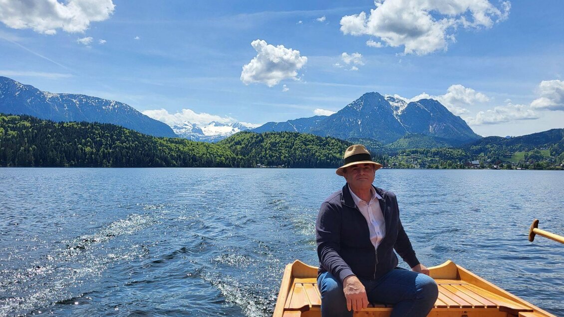 Ein Mann sitzt in einem Boot auf einem klaren See. Im Hintergrund sind grüne Berge und ein blauer Himmel mit weißen Wolken zu sehen. | ©  TVB Ausseerland_Petra Kirchschlager