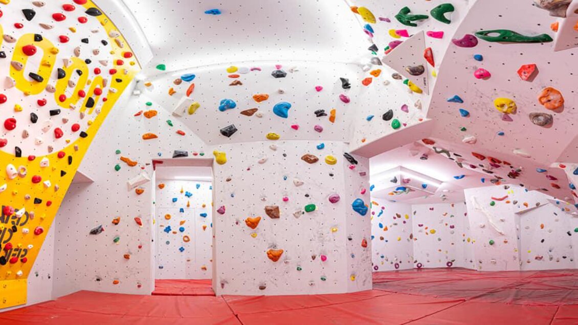 Ein moderner Kletterraum mit bunten Griffen an weißen Wänden. Der Boden ist mit roten Matten ausgelegt, um Sicherheit zu gewährleisten. | © Christoph Huber
