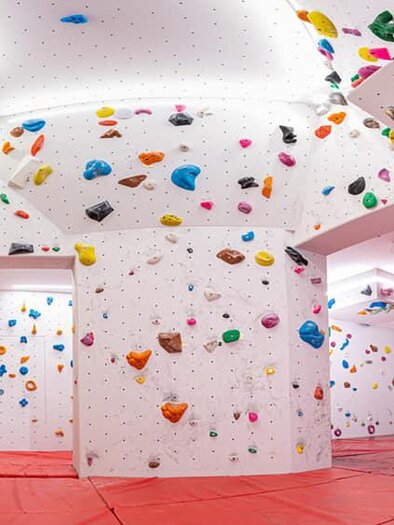 A modern climbing room with colorful holds on white walls. The floor is covered with red mats to ensure safety. | © Christoph Huber