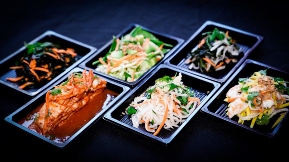 Eine Auswahl an verschiedenen asiatischen Gerichten in schwarzen Behältern. Die Speisen sind bunt dekoriert und enthalten frisches Gemüse und Fisch. | © Bowls & Pots by MayKay