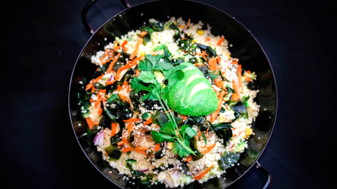 Ein farbenfrohes Gericht mit Couscous, frischem Gemüse und Gewürzen. Obenauf ist eine grüne Avocado und frische Kräuter. | © Bowls & Pots by MayKay