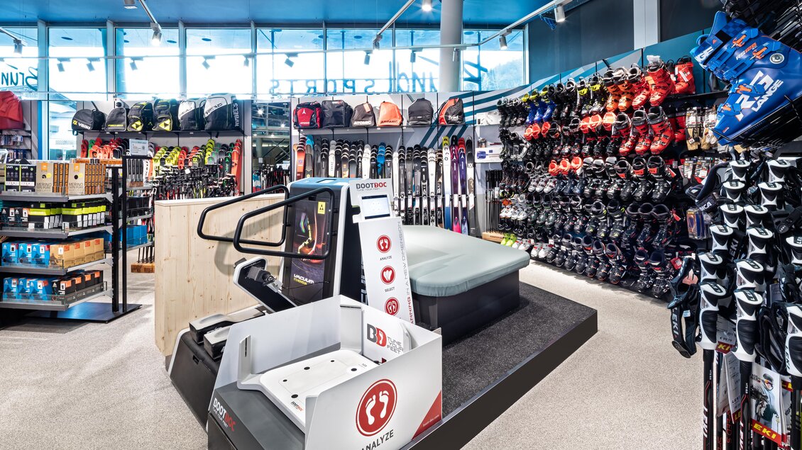 Ein gut sortierter Sportfachgeschäft mit Skiausrüstung und Zubehör. Links sind Regale mit verschiedenen Sportartikeln und rechts finden sich Skischuhe und -ski. | © Bründl Sports/Christian Wöckinger