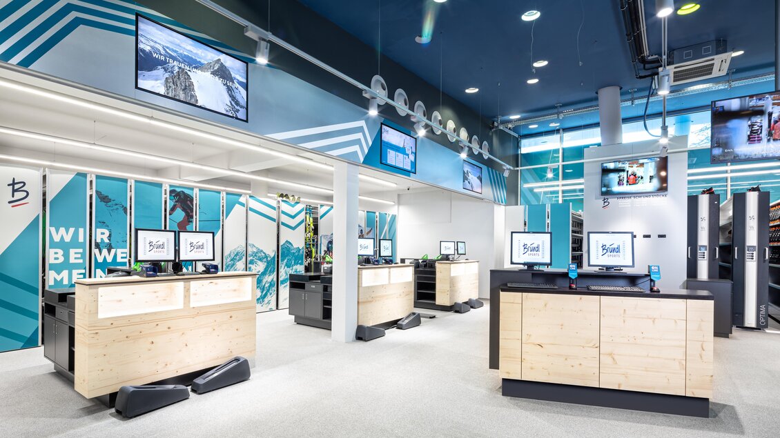 Ein moderner Verkaufsraum mit mehreren Kassen und Bildschirmen. Die Wände sind in einem stilvollen Design mit Bergmotiven gestaltet. | © Bründl Sports/Christian Wöckinger