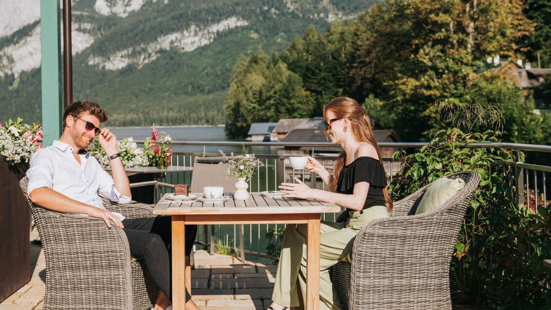 Ein gemütlicher Tisch auf einer Terrasse mit Blick auf einen See und Berge. Ein Mann und eine Frau genießen Kaffee und die sonnige Atmosphäre. | © Karl Steinegger