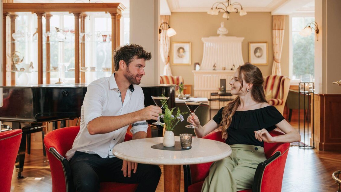 Ein Paar sitzt an einem Tisch in einem eleganten Raum und genießt Getränke. Sie lächeln sich an und wirken entspannt. | © Karl Steinegger