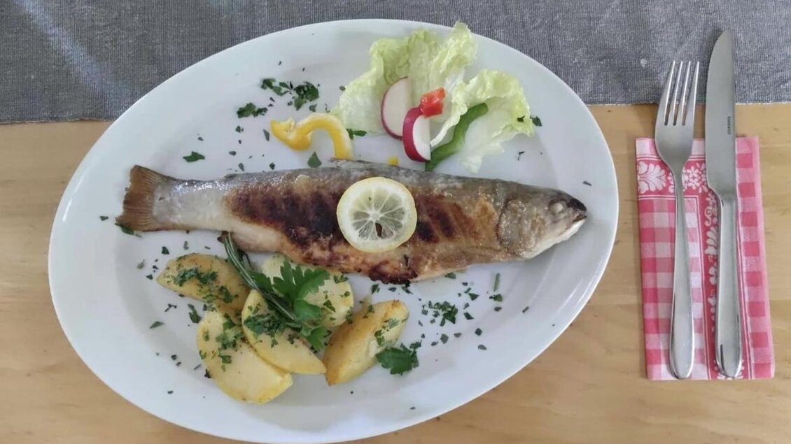 Ein leckerer Fisch mit Zitronenscheibe, serviert auf einem weißen Teller. Dazu gibt es gebratene Kartoffeln und frisches Gemüse. | © Breitlahnhütte