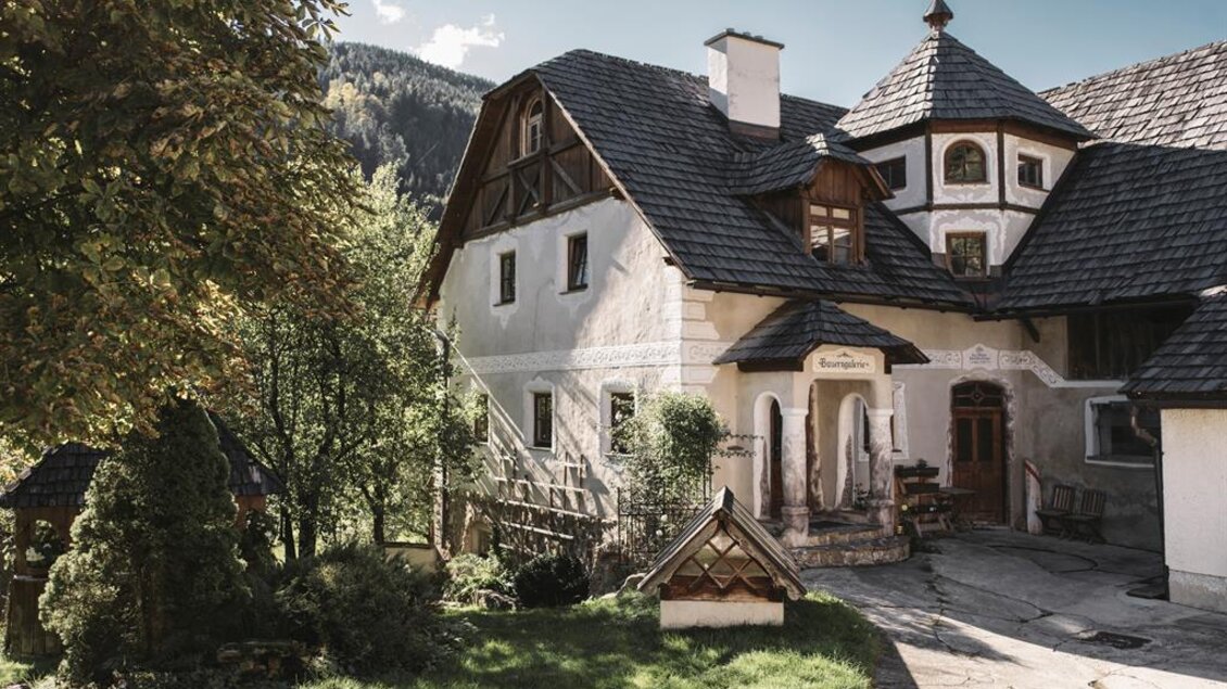 Ein charmantes Landhaus umgeben von Bäumen und Wiesen. Im Hintergrund sind sanfte Hügel und ein klarer Himmel sichtbar. | © Stefan Leitner