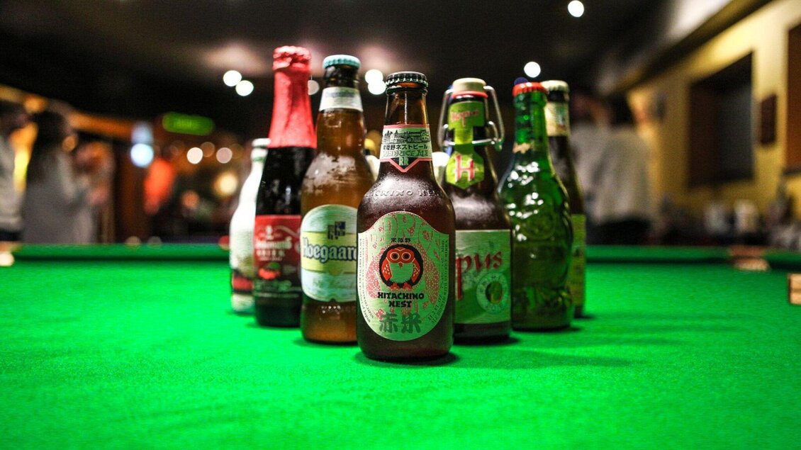 Eine Auswahl von Bierflaschen steht auf einem grünen Tisch. Der Hintergrund ist unscharf und zeigt eine gesellige Atmosphäre. | © Brot & Spiele