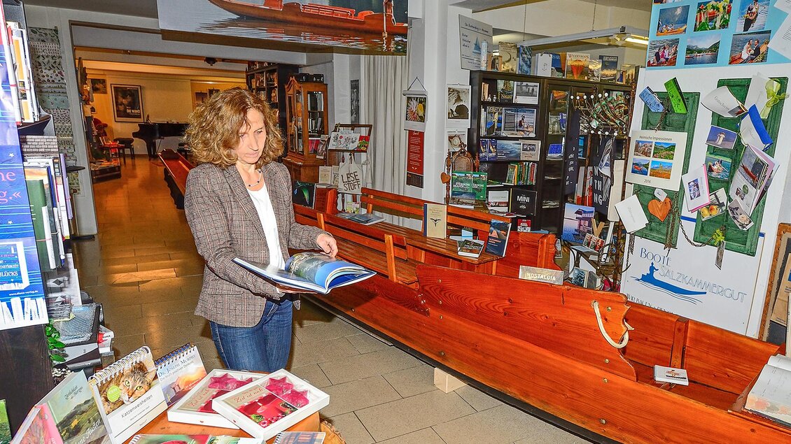 Eine Frau betrachtet ein Buch in einem Ausstellungsraum mit einem Holzboot im Hintergrund. Der Raum enthält verschiedene Informationen und Materialien über Bootsaktivitäten. | © Herfried Marek