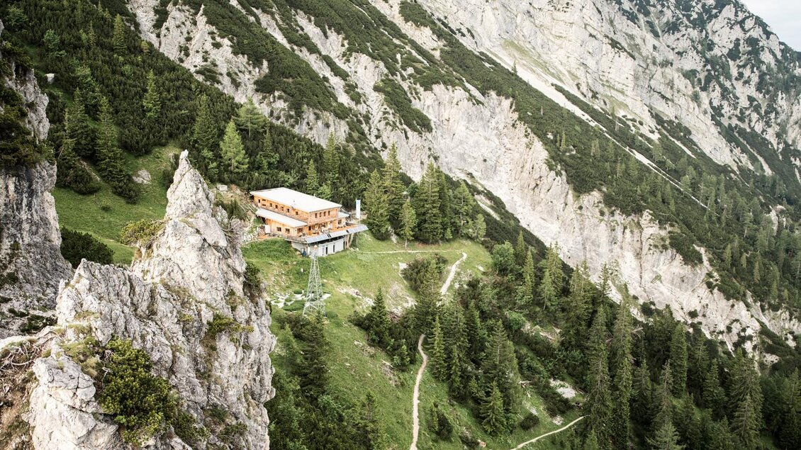 Ein malerisches Bergpanorama mit steilen Felsen und grünen Wäldern. Im Vordergrund steht eine Berghütte, umgeben von Wanderwegen. | © Stefan Leitner
