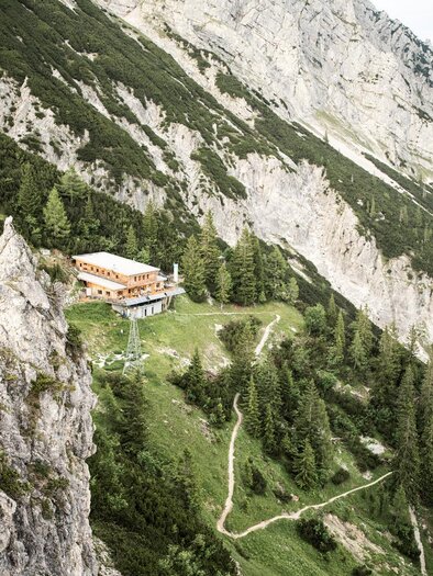 A picturesque mountain panorama with steep cliffs and green forests. In the foreground stands a mountain cabin, surrounded by hiking trails. | © Stefan Leitner
