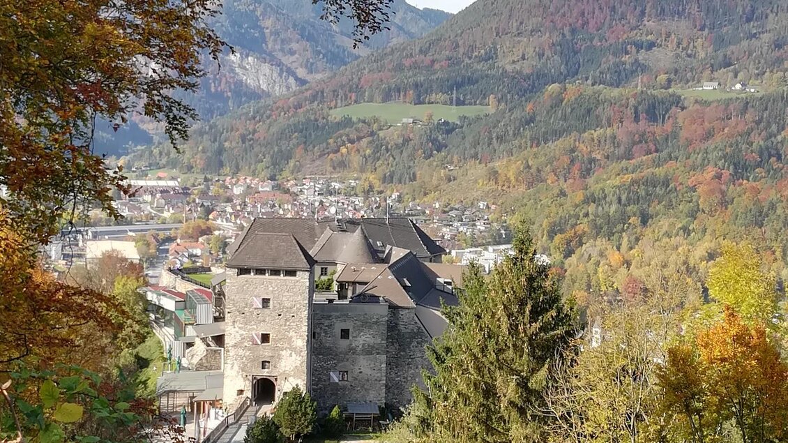 Eine malerische Burg umgeben von herbstlichen Bäumen und Bergen. Im Hintergrund sieht man eine idyllische Landschaft mit bunten Blättern. | © TV Kapfenberg