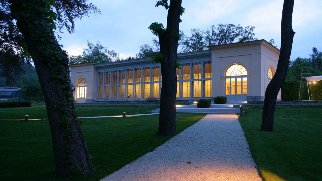Beleuchtete Orangerie mit großen Rundbogenfenstern im Burggarten Graz | © Graz Tourismus-Harry Schiffer
