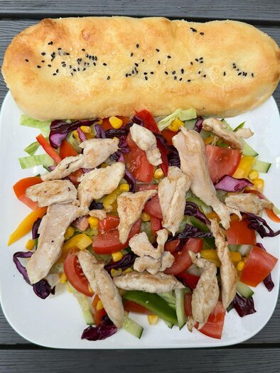 Ein frischer Salat mit Gemüse und gebratenem Hähnchenfleisch. Dazu ein knuspriges Brot. | © Kevin Sönmez