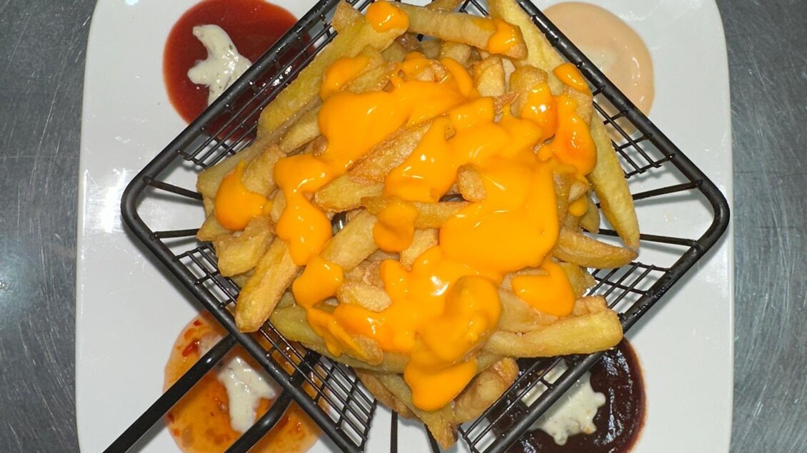 Frittierte Pommes mit reichlich Käsesoße in einem kleinen Korb. Dazu drei verschiedene Saucen auf einem Teller. | © Kevin Dönmez