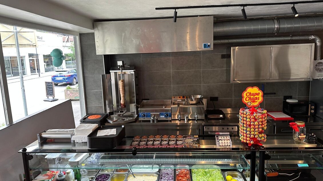 Eine moderne Küchenzeile mit verschiedenen frischen Zutaten und Kochgeräten. Im Vordergrund sind bunte Zutaten auf einer Glasvitrine angeordnet. | © Kevin Dönmez