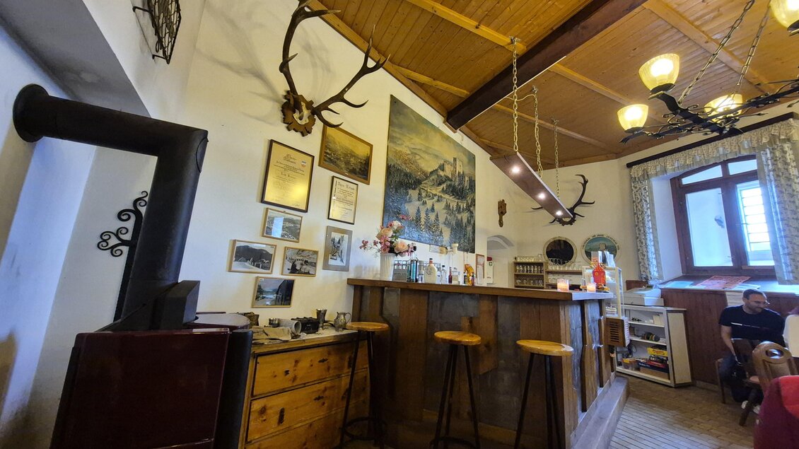 Eine gemütliche Bar mit Holzregal und Hockern. An den Wänden hängen Bilder und Dekorationen, während der Raum warm und einladend wirkt. | © Andrea Stelzer