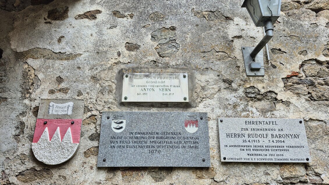 Eine historische Wand mit verschiedenen Plaketten und einem Wappen. Neben den Schildern hängt eine kleine Lampe. | © Andrea Stelzer