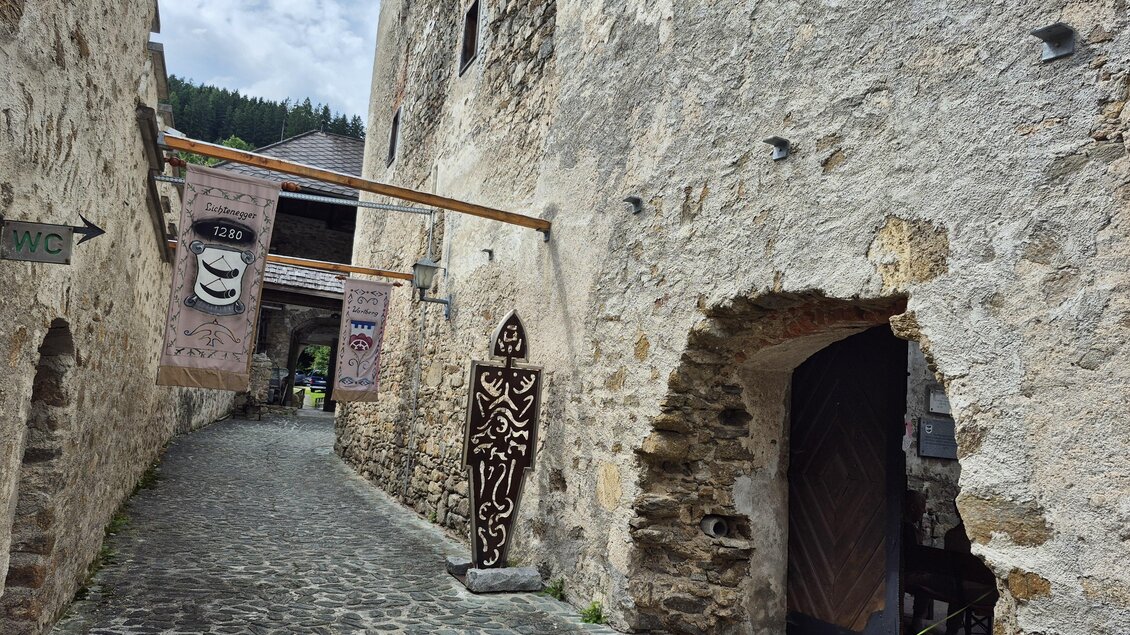 Eine schmale, gepflasterte Gasse zwischen alten Steingebäuden. An der Wand hängt ein Kunstwerk und ein kleiner Hund läuft vorbei. | © Andrea Stelzer