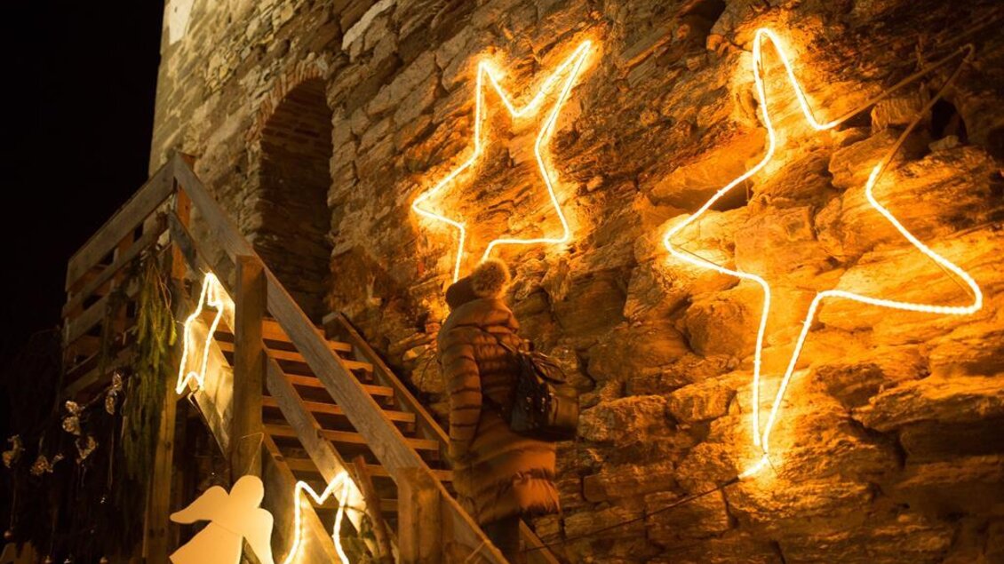 Eine stimmungsvolle Nachtaufnahme mit leuchtenden Sternen und Engeln an einer Steinmauer. Eine Person geht die Treppe hinauf, umgeben von festlicher Beleuchtung. | © Kump.Photography