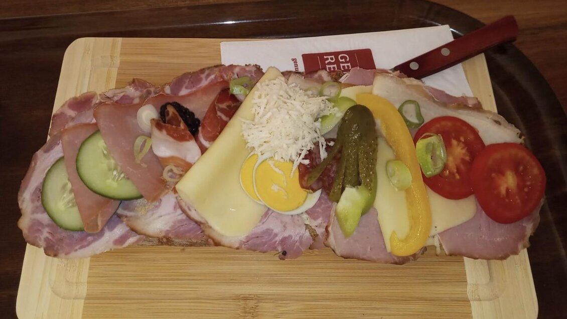 Ein belegtes Brot mit verschiedenen Aufschnitt, Käse und frischem Gemüse. Es ist dekorativ angerichtet auf einem Holzbrett. | © Fam. Tomaschitz