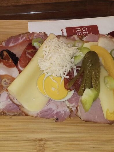 A sandwich with various cold cuts, cheese, and fresh vegetables. It is decoratively arranged on a wooden board. | © Fam. Tomaschitz