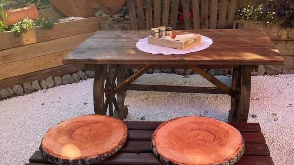 Ein rustikaler Holztisch mit zwei Sitzbänken aus Holzscheiben. Die gemütliche Gartenumgebung ist von Pflanzen umgeben. | © Fam. Tomaschitz